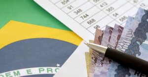 Imagem com caneta, bandeira do Brasil e algumas notas. Fazem alusão ao tema central: Endividamento no Brasil em 2022.