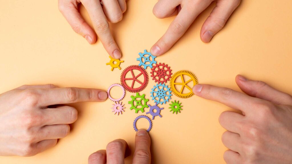 Imagem com várias mãos montando engrenagens juntas, representando o efeito da psicologia organizacional na organização.