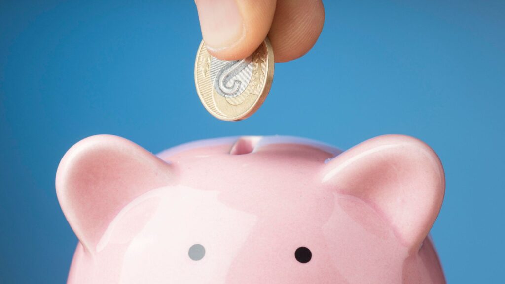 Cofre em formato de porco recebendo moeda, representando a poupança. Sabendo qual é o seu perfil financeiro, você consegue listar metas mais realistas e estratégias para poupar.