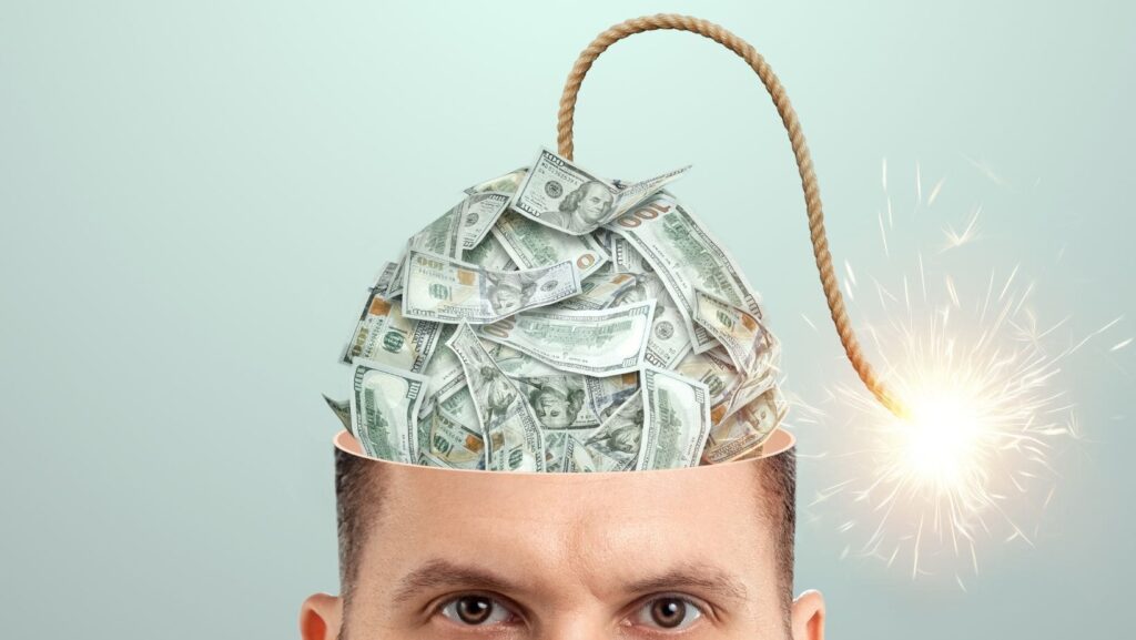 Homem com várias cédulas de dinheiro na cabeça e uma ponta indicando ser uma bomba, aludindo à necessidade de mudança da mentalidade financeira para que o assunto finanças não se torne uma bomba prestes à explodir.